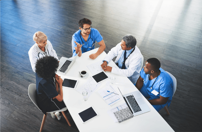 Medical professionals collaborating around a table with laptops and documents